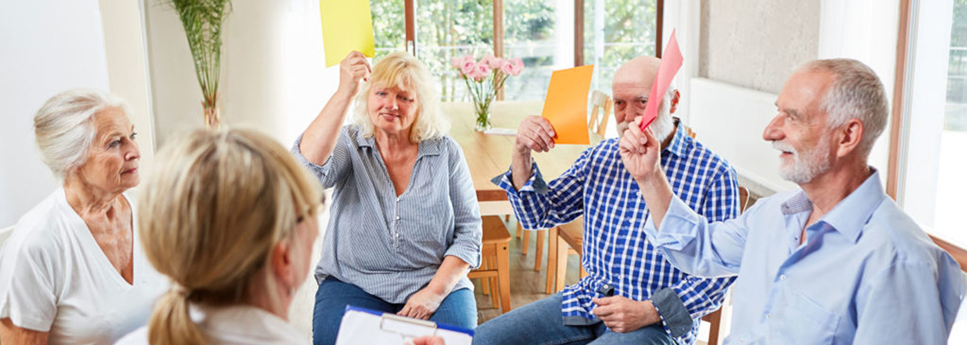 Fünf Senioren sitzten im Kreis, zwei Personen halten farbige Karten hoch.
