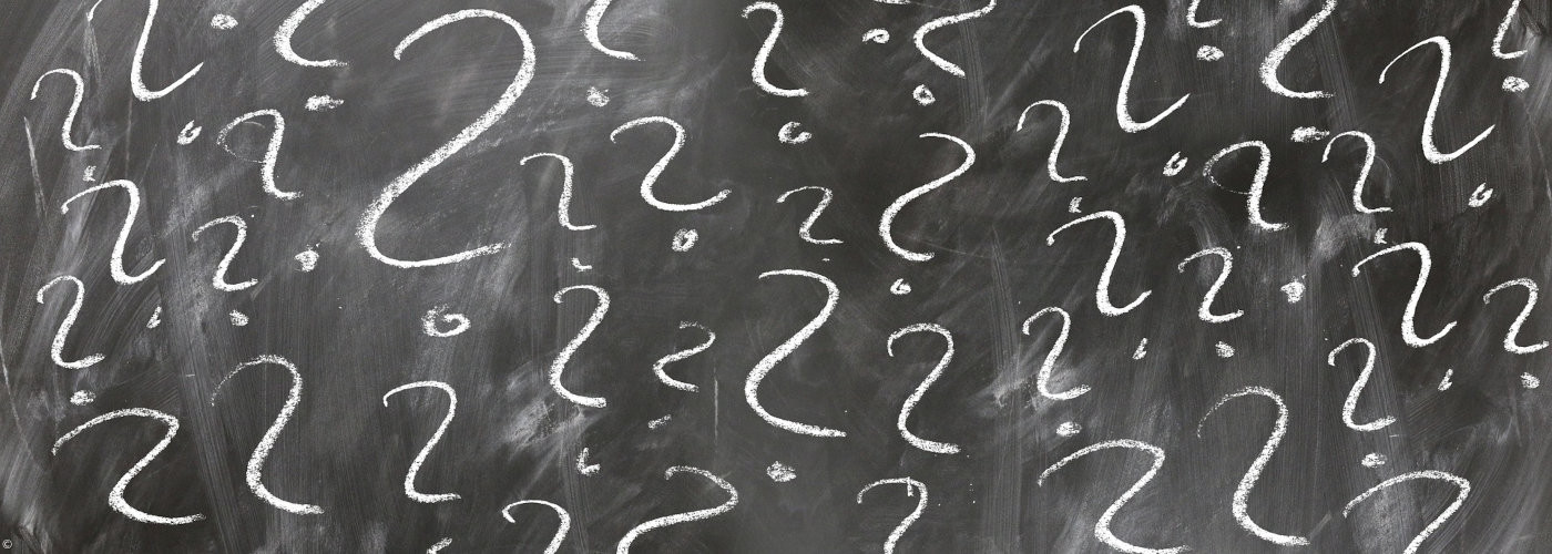 Schwarze Schultafel mit weißen Fragezeichen in verschiedenen Größen, gleichmäßig über die Fläche verteilt.