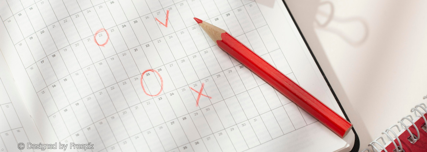 Roter Buntstift liegt auf einem Kalenderblatt mit handschriftlichen Kreisen und Kreuzen