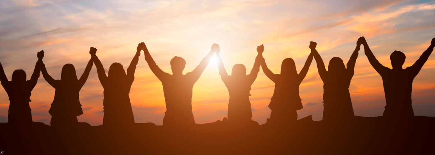 Schattenriss von acht Personen, die sich an den Händen halten, vor einem Sonnenuntergang