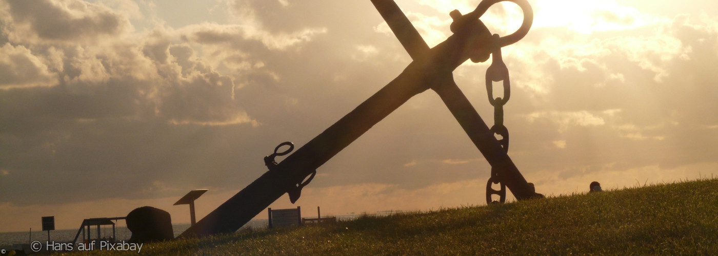 Große Anker mit Kette auf einem Hügel vor bewölktem Himmel bei Sonnenuntergang