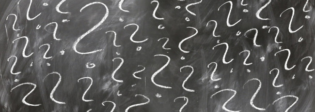 Schwarze Schultafel mit weißen Fragezeichen in verschiedenen Größen, gleichmäßig über die Fläche verteilt.