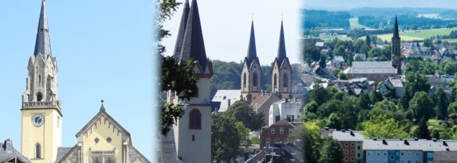 Blick auf mehrere Kirchtürme und Wohnhäuser in einer grünen Stadtlandschaft unter blauem Himmel