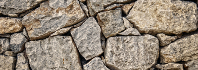 Mauerwerk aus unregelmäßig geformten grauen und beige Steinen, die übereinander gestapelt sind.